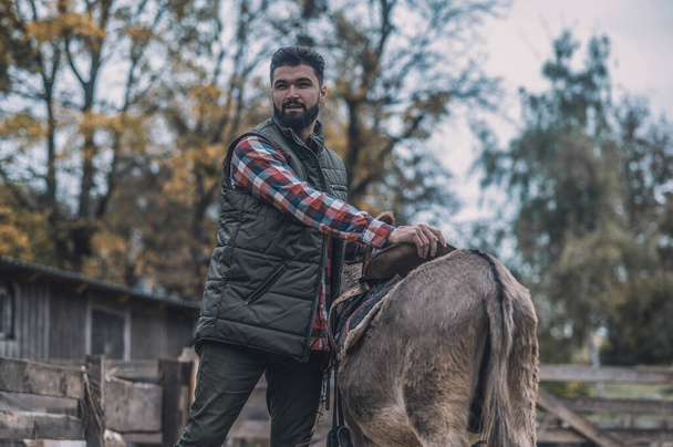 A dark-haired man saddling up a donkey - Foto, afbeelding