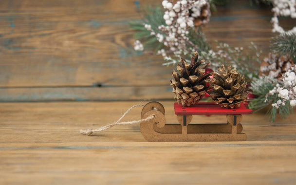 Παιδικό ξύλινο έλκηθρο σε ξύλινο φόντο με κουκουνάρι, αντιγραφή χώρου. Κάρτα νέου έτους. - Φωτογραφία, εικόνα