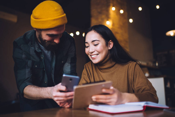 Man with beard showing young woman in casual clothes screen of smartphone while female taking notes using clipboard and notebook - Foto, Imagem