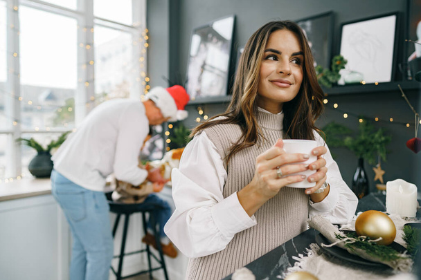 Attractive young woman drinks tea in the kitchen for Christmas - Fotografie, Obrázek