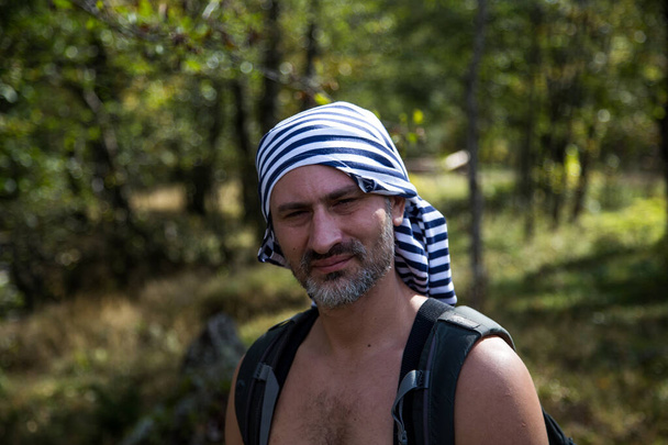 アクティブな男性スポーティな男の肖像画屋外ハイキング。髭と包帯をした若い男性観光客、バックパックを屋外で身に着けている彼の頭の上にカーチーフ. - 写真・画像