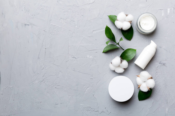 Organic cosmetic products with cotton flower and green leaves on cement background. Copy space, flat lay. - Photo, Image
