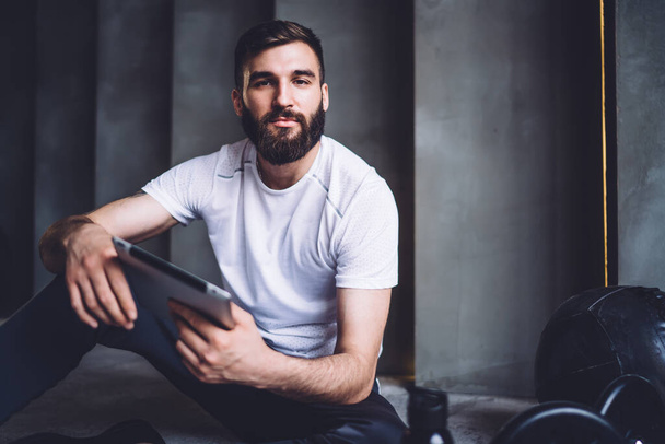 Half length portrait of handsome male athlete using modern digital tablet for blogging and share content, young sportsman in trendy activewear holding touchpad for using applications and blogging - Foto, Imagen
