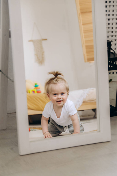 A cute baby smiles and crawls on the floor near the mirror in the house. Cheerful kid is playing in the room. - Photo, Image