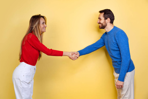 Cropped portrait of young couple, man and woman, shaking eatch other hands isolated over yellow background - Photo, Image