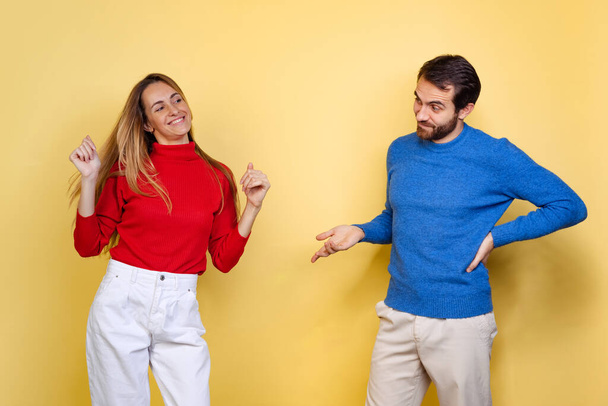 Cropped portrait of young couple, man looking at dancing woman in misunderstanding isolated over yellow background - Foto, Imagem
