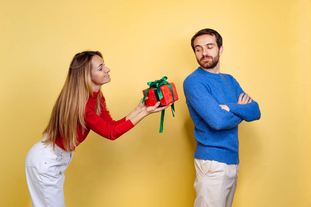 Cropped portrait of couple, woman giving man his holiday present isolated over yellow background. Merry winter holidays - Foto, Bild