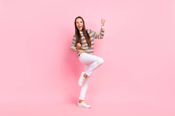 Photo of lucky pretty young woman wear dotted sweater smiling walking rising fists isolated pink color background - Foto, afbeelding