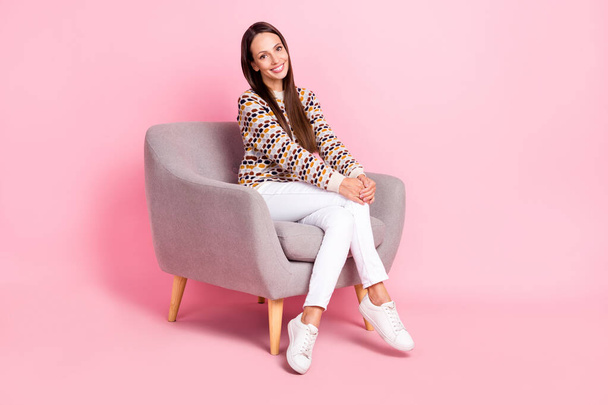 Photo of shiny adorable young woman wear dotted sweater smiling sitting cozy armchair isolated pink color background - Фото, зображення