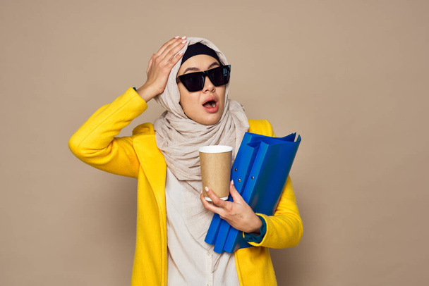 woman in sunglasses in hijab a cup of coffee beige background - Фото, зображення