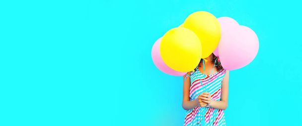 Woman covering her head with bunch of colorful balloons on a blue background - Zdjęcie, obraz