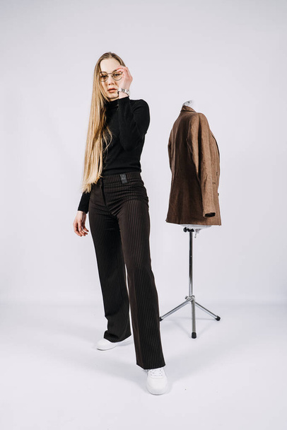 Young woman, fashion designer, stylist full-length casual style portrait. Fashionable woman in black turtleneck and brown jacket. Studio shot of stylish blonde girl with long hair in casual clothes. - Φωτογραφία, εικόνα