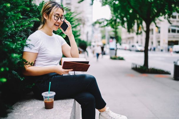 Charming woman in optical eyewear using roaming connection for discuss travel planning on leisure, beautiful Japanese female student with education notepad phoning via cellular application - Foto, Bild