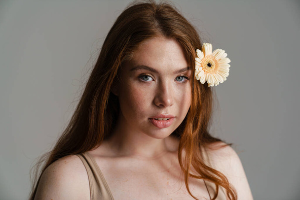 Close up portrait of a young white woman with long hair posing with a flower over gray background - Fotoğraf, Görsel