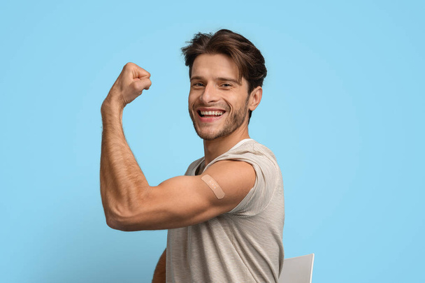 Hombre joven vacunado demostrando bíceps con banda adhesiva después de la inyección - Foto, Imagen