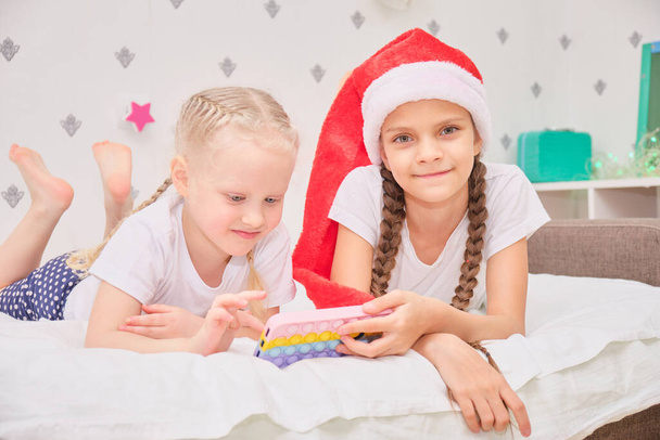 two cute girls lie on the bed and play smartphone games, christmas holidays concept, video call to relatives for merry christmas, festive decor and mood - Foto, imagen
