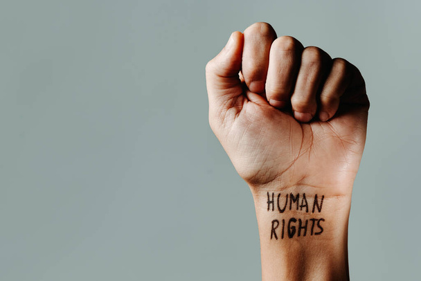 il pugno sollevato di un uomo con il testo diritti umani scritto al polso, su uno sfondo grigio con qualche spazio vuoto a sinistra - Foto, immagini