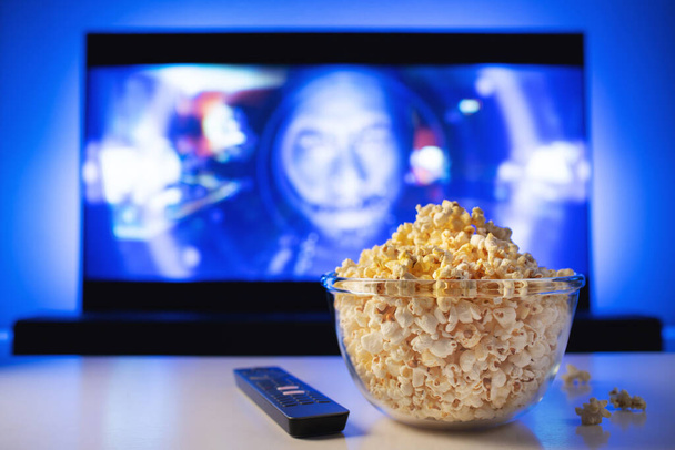eine Glasschale Popcorn und Fernbedienung im Hintergrund funktioniert der Fernseher. abends gemütlich einen Film oder eine Fernsehserie zu Hause anschauen. - Foto, Bild