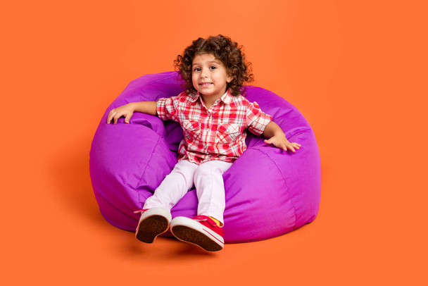 Full body photo of cute little brunette girl sit wear shirt pants shoes isolated on orange color background - 写真・画像