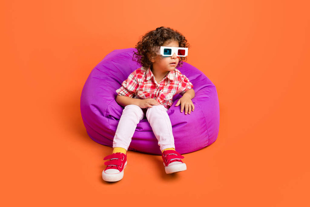 Photo of adorable impressed schoolgirl wear plaid outfit 3d glasses sitting bean bag isolated orange color background - Fotografie, Obrázek