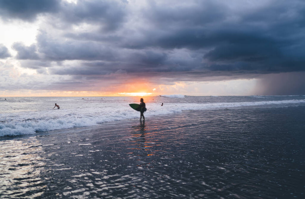 Anonymous distant traveler with surfboard strolling along waving seashore while preparing for tide to swim in sunset time in overcast - Фото, изображение