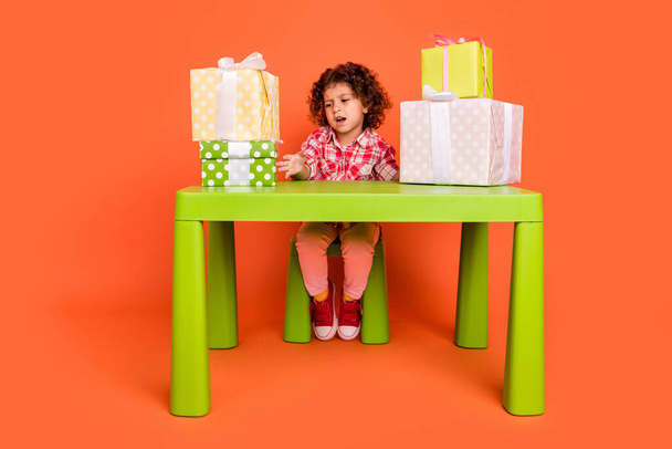 Photo of moody upset schoolgirl wear plaid outfit sitting green table dislike gifts boxes isolated orange color background - Foto, Imagem