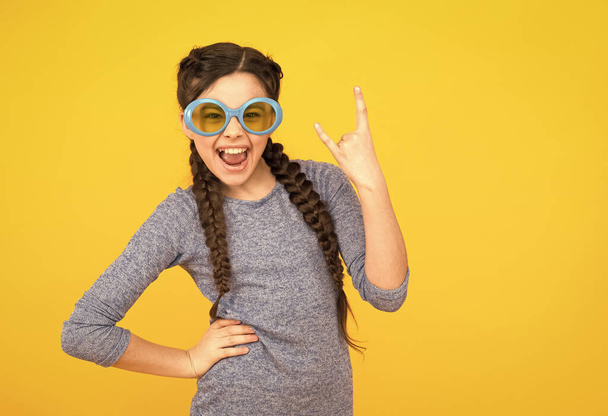 happy child girl has fashionable hairstyle in glasses on yellow background, ready for vacation - Foto, immagini