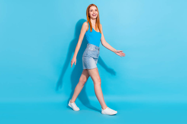 Photo portrait red haired woman in pretty singlet jeans skirt walking forward isolated pastel blue color background - Foto, Bild