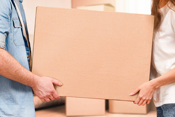 un uomo e una donna portano in mano una scatola di cartone e si trasferiscono in una nuova casa - Foto, immagini