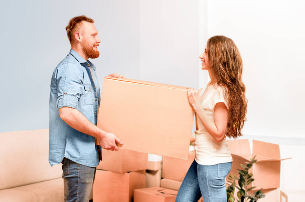 счастливая молодая пара нести картонную коробку в руках при переезде в новый дом - Фото, изображение