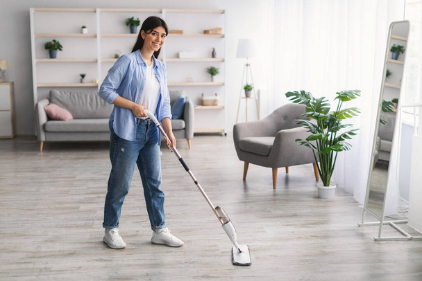 Mujer alegre limpieza piso con aerosol fregona en salón eoom - Foto, imagen