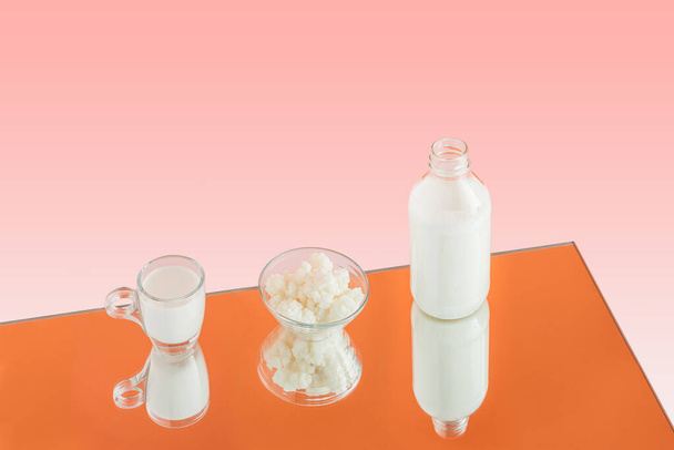 Palack, kefir tej és tál kefir szemek tükröződnek egy tükörben elszigetelt narancssárga alapon. Minimális tejtermék természetes egészséges étel jelenet. Emésztőital vagy probiotikumok forráskoncepciója.  - Fotó, kép