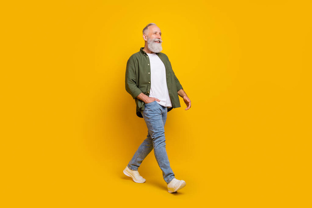 Full length body size side profile photo of senior man smiling walking forward isolated vibrant yellow color background - Foto, Imagen