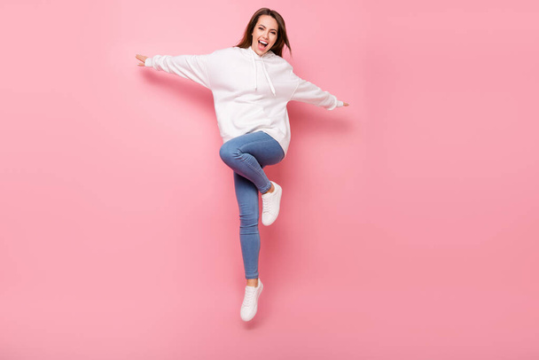 Photo of sweet adorable young lady wear white hoodie smiling jumping high hands sides isolated pink color background - Photo, image
