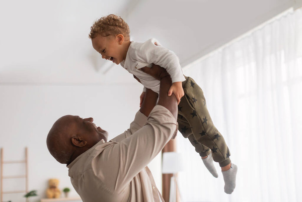 Afrikai nagyapa tartja a kis unokáját a levegőben otthon - Fotó, kép