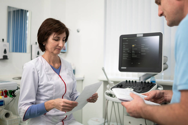 Lääkäri kardiologi ultraäänidiagnostiikan toimistossa potilaan kanssa tutkii lääketieteellisiä testejä nykyaikaisen klinikan terveystarkastuksen aikana. Lääketieteellinen konsultointi. terveydenhuolto, sairaanhoito - Valokuva, kuva