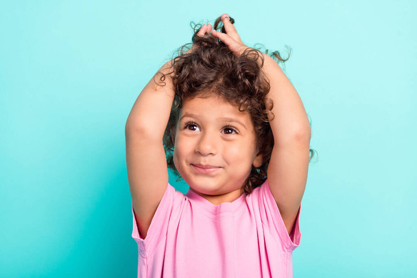 Fénykép a fiatal kis latin lány boldog pozitív mosoly kezét érintse meg a haj néz üres tér elszigetelt türkiz szín háttér - Fotó, kép