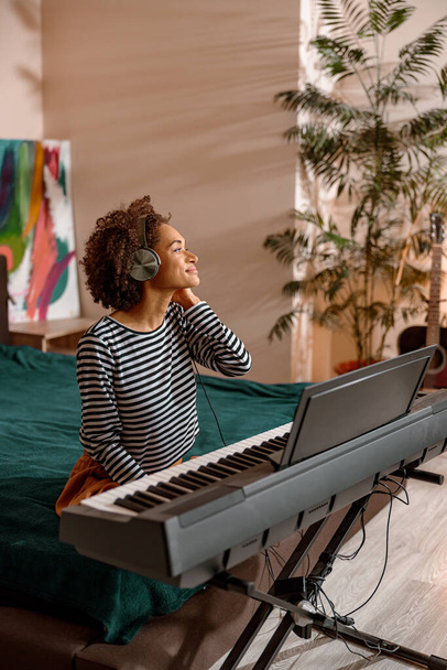 Γυναίκα μουσικός σε ακουστικά παίζει synthesizer στο σπίτι - Φωτογραφία, εικόνα