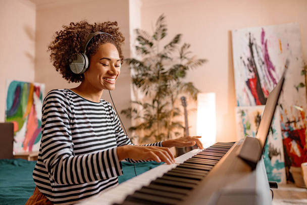 Χαρούμενη νεαρή γυναίκα παίζει synthesizer στο σπίτι - Φωτογραφία, εικόνα
