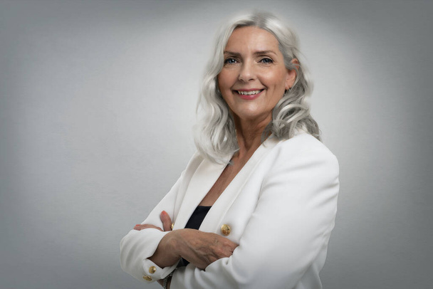 Studio shot of grey haired senior woman wearing elegant clothes while standing at isolated grey background. Copy space. - Foto, immagini