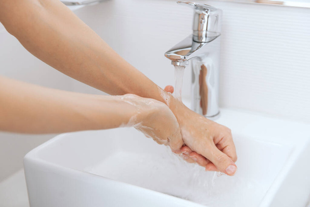 Washing hands under the flowing water tap. Hygiene concept hand detail. Washing hands rubbing with soap for corona virus prevention, hygiene to stop spreading corona virus in or public wash room - Foto, afbeelding