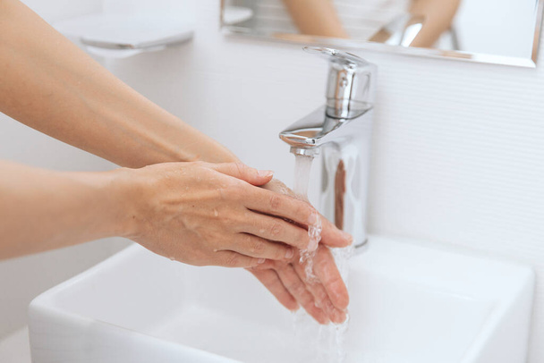 Washing hands under the flowing water tap. Hygiene concept hand detail. Washing hands rubbing with soap for corona virus prevention, hygiene to stop spreading corona virus in or public wash room - Photo, image
