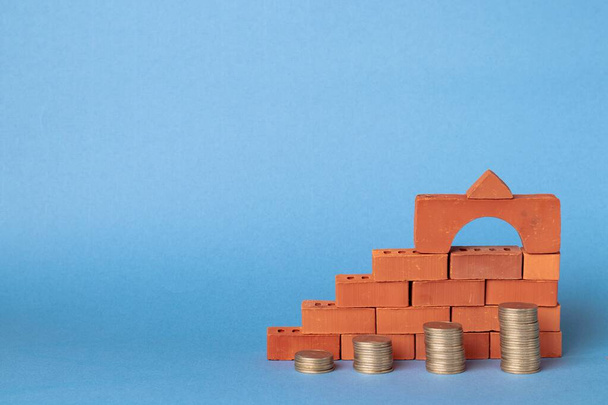 Stacks of coins in the form of steps against a background of blocks of red bricks. Investment in construction - Photo, Image