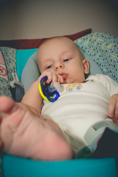 Two months old baby boy is lying in infant car seat and holds pacifier in little hand - Photo, image