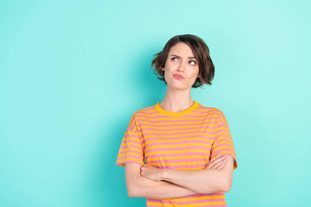 Photo of thoughtful doubtful young woman dressed striped t-shirt looking empty space arms folded isolated teal color background - Фото, зображення
