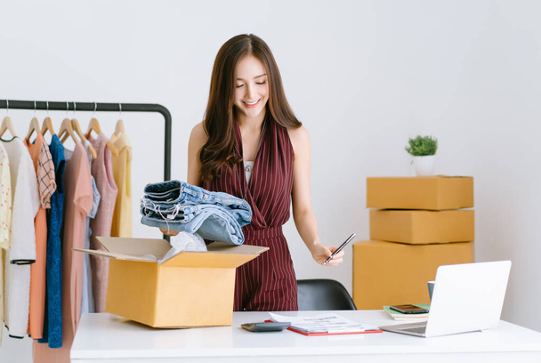 Beautiful Female Entrepreneur Asian casual woman SME small business checking order and packing products to cardboard box to customer. Freelance work, business ideas online. SME marketing concept - Photo, Image