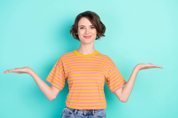 Photo of pretty adorable young woman dressed striped t-shirt showing arms scales empty space smiling isolated teal color background - Foto, imagen