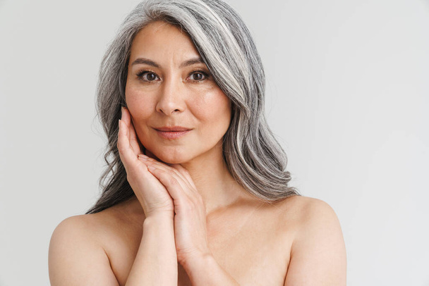 Mature shirtless woman with grey hair posing and looking at camera isolated over white background - Фото, изображение