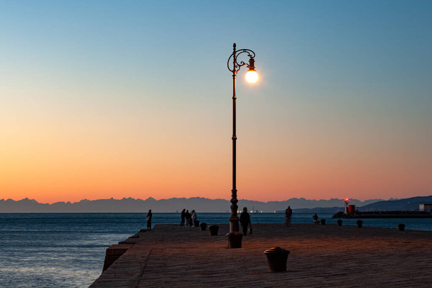 View of the illuminated street lantern in the Molo Audace pier of Trieste in a winter evening  - Photo, Image