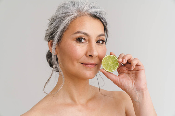 Mature shirtless woman with grey hair showing lime isolated over white background - Photo, image